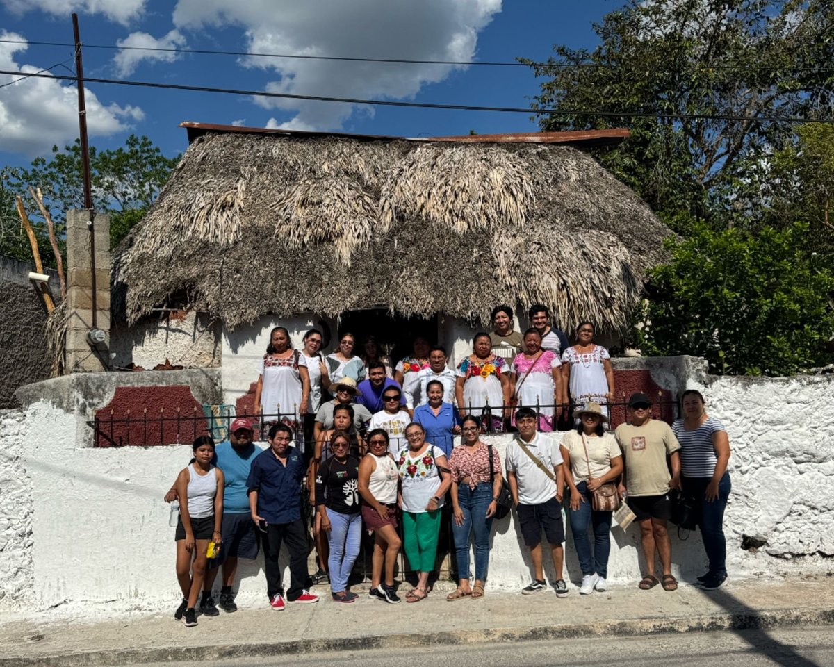 Group of people standing in front of a traditional thatched-roof house with white walls